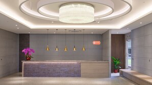 Un espace d’accueil moderne avec un comptoir central, des luminaires suspendus et un grand lustre.