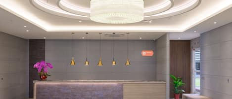 A modern reception area with a central desk, pendant lighting, and a large chandelier.