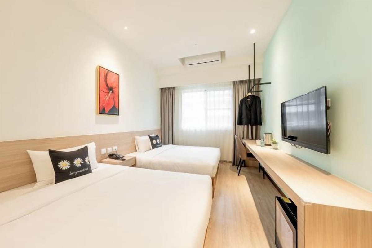 A hotel room with two beds, a TV, a desk, and a window with curtains.