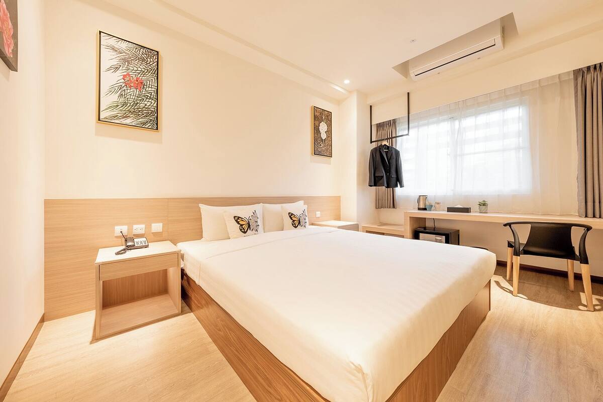 A hotel room with a large bed, a desk, a chair, and a wardrobe.