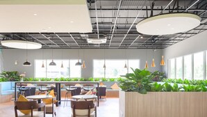 Un espace intérieur moderne doté d’un plancher en bois, de tables et de chaises rondes, de grandes fenêtres et de plantes d’intérieur.