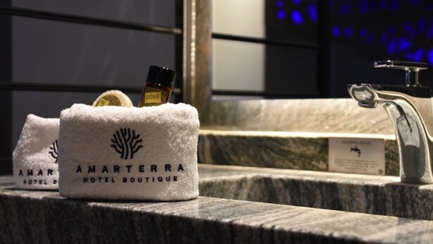 A bathroom counter with a towel dispenser containing a bottle of DOOR body spray and a towel branded with "AMARTEERRA HOTEL BOUTIQUE". - Amarterra Hotel Boutique (Mexico City)
