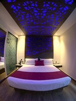 Una habitación de hotel moderna con una cama grande, un techo decorativo y una mesita de noche con lámpara.
