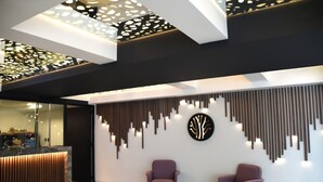 A modern reception area with a reception desk, two purple armchairs, and a decorative wall with vertical elements and a circular design. - Amarterra Hotel Boutique (Mexico City)