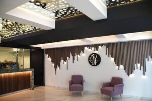 Un área de recepción moderna con un mostrador, dos sillones morados y una pared decorativa con elementos verticales y un diseño circular.