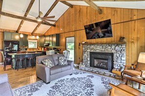 A spacious living room with a stone fireplace, wooden ceiling beams, a large TV, and a bar area with stools. - Lake Santeetlah Escape w/ Kayaks, Boat Slip & More (Robbinsville)