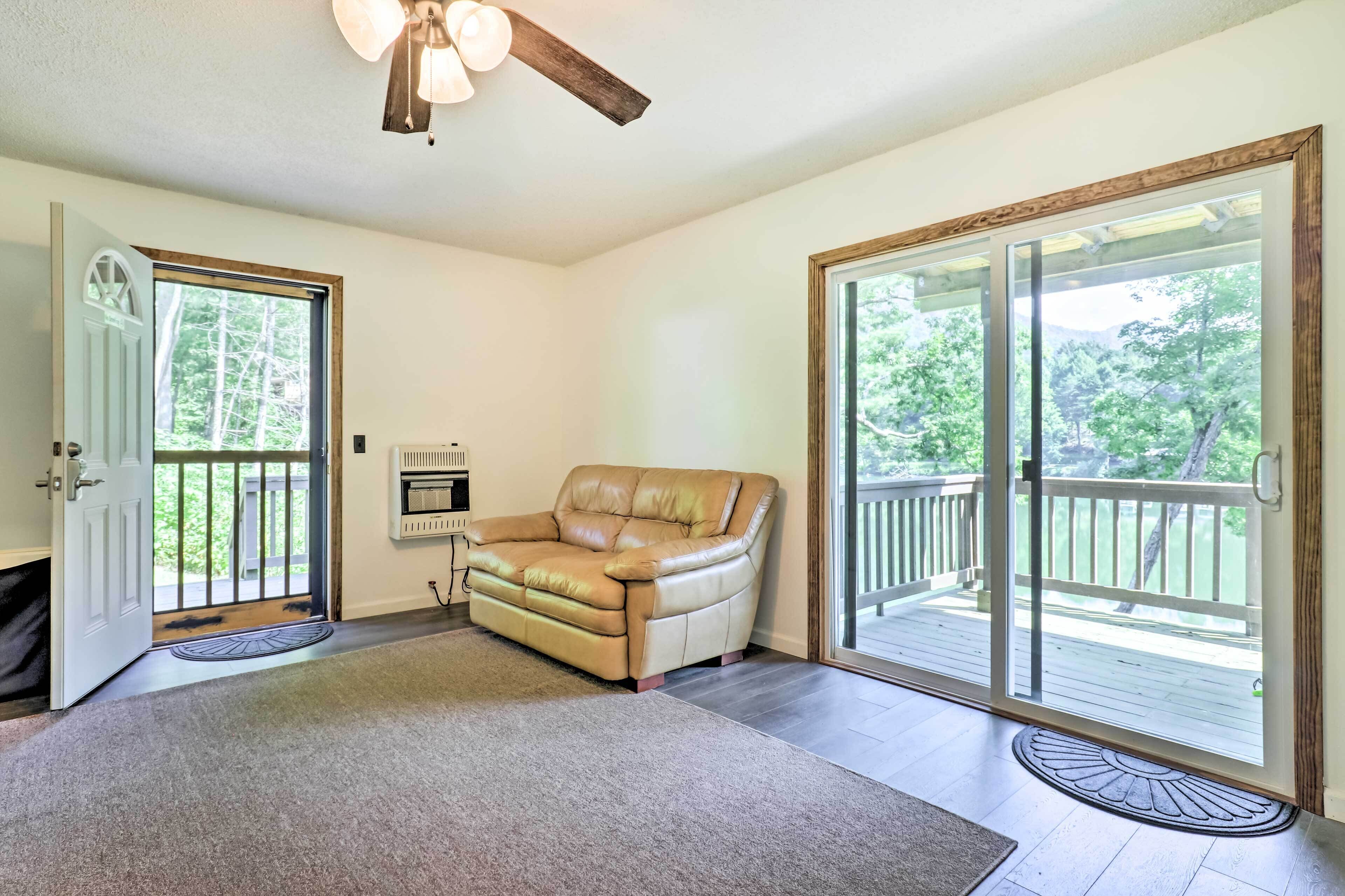 A spacious room with a beige leather sofa, a ceiling fan, and a sliding glass door leading to a deck.