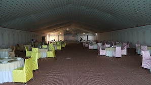 Une grande salle avec des tables rondes et des chaises, un plafond haut orné de motifs et un sol en briques.