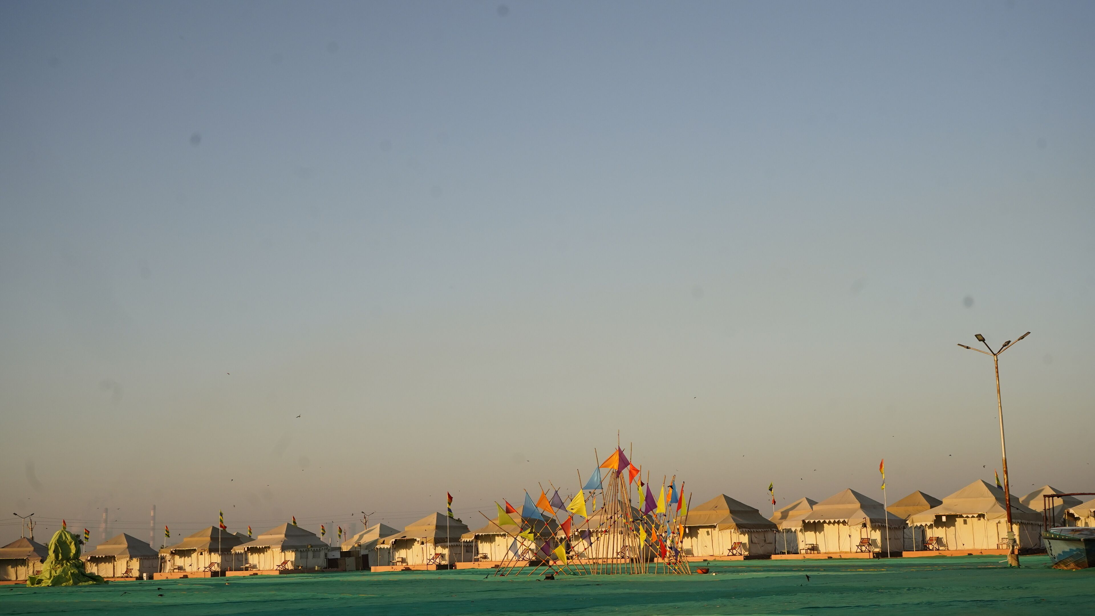 A row of white tents with a row of colorful flags in front.