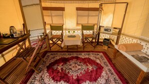 Une pièce chaleureuse avec une table en bois, deux chaises, un tapis rouge à motifs et un lit recouvert d’une courtepointe à motifs.