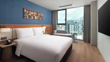 A hotel room with a large bed, a desk with a phone, a chair, a small table, a TV, and a city view.