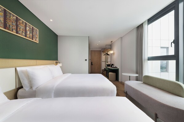 Une chambre d’hôtel avec deux lits, un coin salon, une petite table, un miroir et une fenêtre.