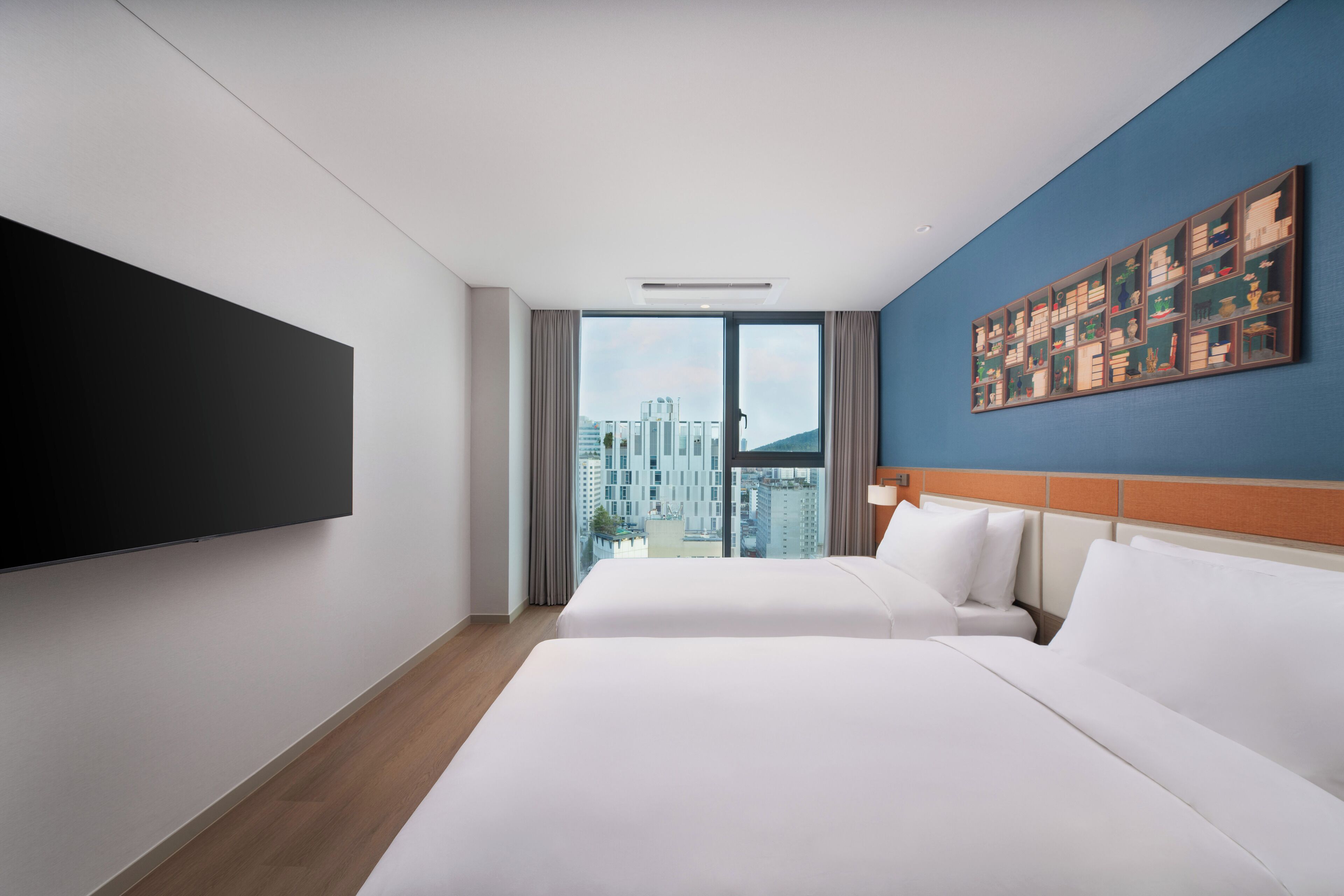 Habitación de hotel con dos camas, un ventanal grande, un televisor de pantalla plana y una obra de arte colgada en la pared.