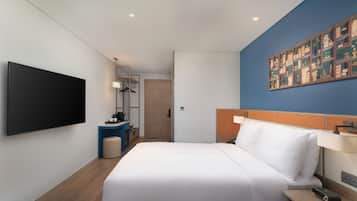 Une chambre d’hôtel moderne dotée d’un grand lit, d’un téléviseur à écran plat, d’un bureau avec une chaise et d’une étagère murale agrémentée d’objets décoratifs.