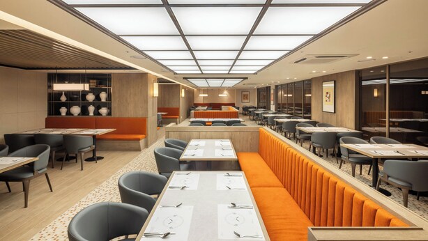 A modern restaurant with high ceilings, recessed lighting, and a mix of booth and table seating.