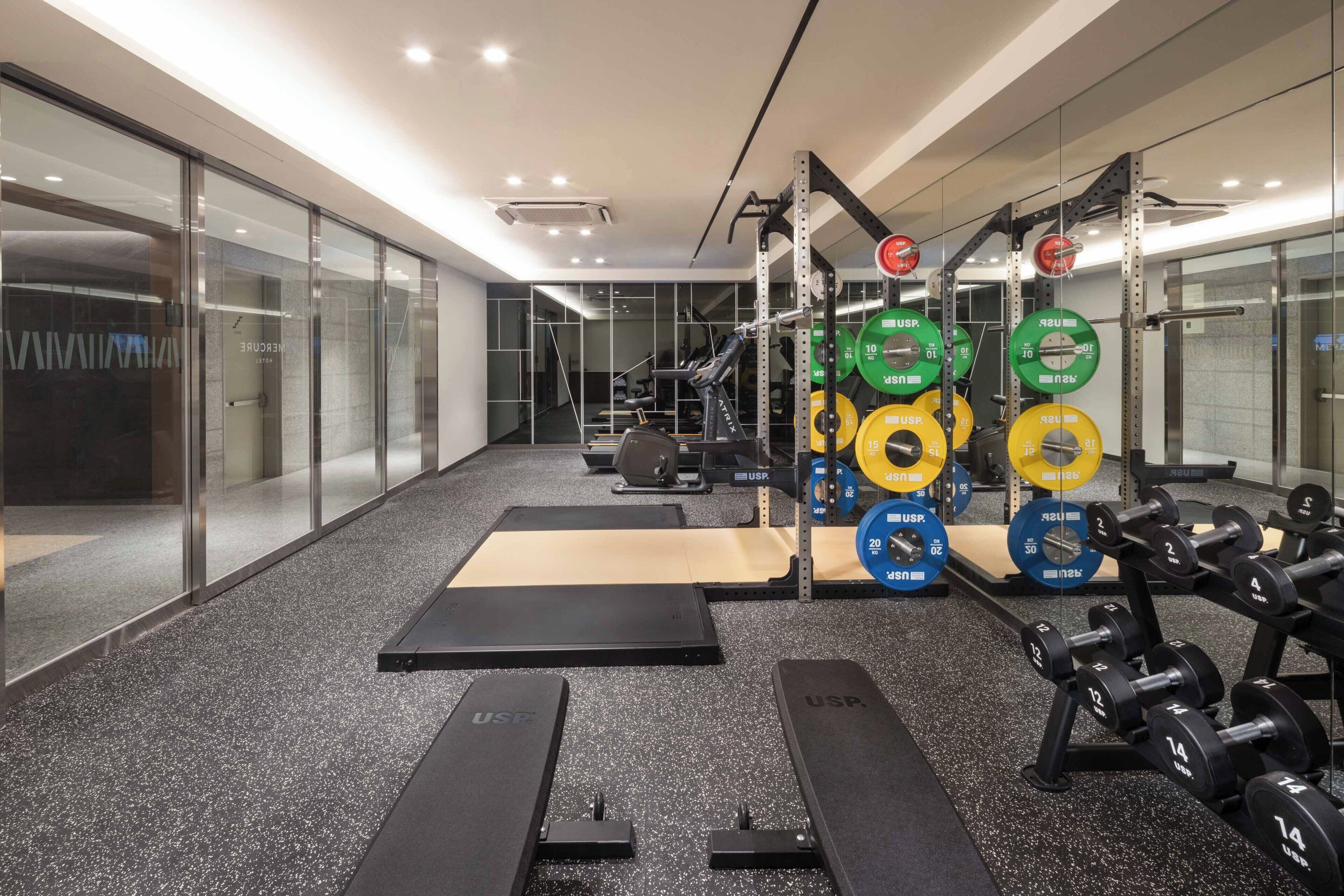 A gym with weightlifting equipment, treadmills, and a mirrored wall.
