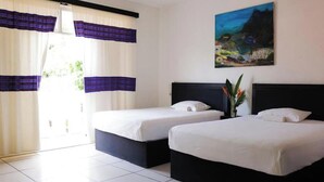 A hotel room with two beds, a painting on the wall, and curtains.