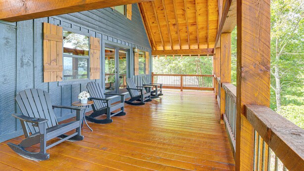 Een houten terras met Adirondack-stoelen en een tafel, met uitzicht op een bebost gebied.