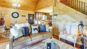 Een gezellig interieur van een chalet met een leren bank, een eethoek en een trap naar een zolder.