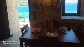Un coin repas avec une table dressée pour deux personnes, un vase contenant des plumes d’herbe des pampas et une vue sur la mer par la fenêtre.