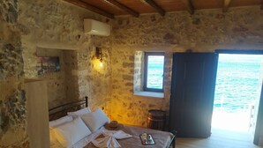 Une pièce rustique en pierre, avec un lit, une petite table et une fenêtre donnant sur la mer.