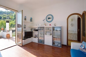 Un salón con televisor, estanterías, un reloj y vistas al verdor.