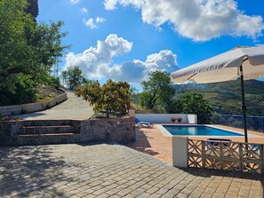 Zona de piscina con un sendero de piedra, un árbol pequeño y vistas a colinas al fondo.