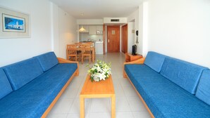 A living room with two blue sofas, a wooden coffee table, and a dining area with a wooden table and chairs. - Apartment Hotel Maracaibo Standard with Pool, Wi-Fi & Terrace (Can Picafort)