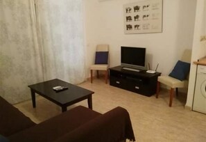 Un soggiorno con divano, tavolino, televisore su supporto e lavatrice.