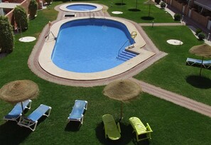 Una piscina con bordo circostante, poltrone sdraio e un piccolo giardino.