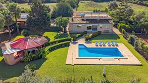 Uma casa com piscina, estrutura com telhado vermelho e gramado bem cuidado.