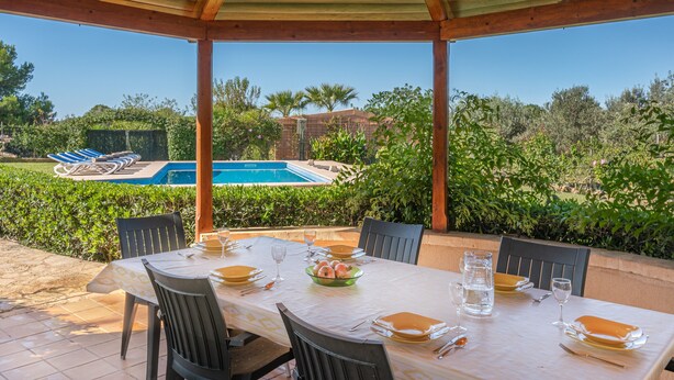 Uma área de refeições ao ar livre com vista para a piscina, terraço coberto e mesas bem arrumadas.