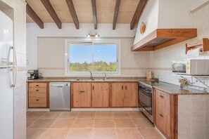 Cocina con armarios de madera, lavavajillas, estufa y ventana con vista a espacios verdes.