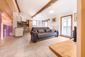 A cozy living area with a sofa, wooden beams, a kitchen, and a balcony.