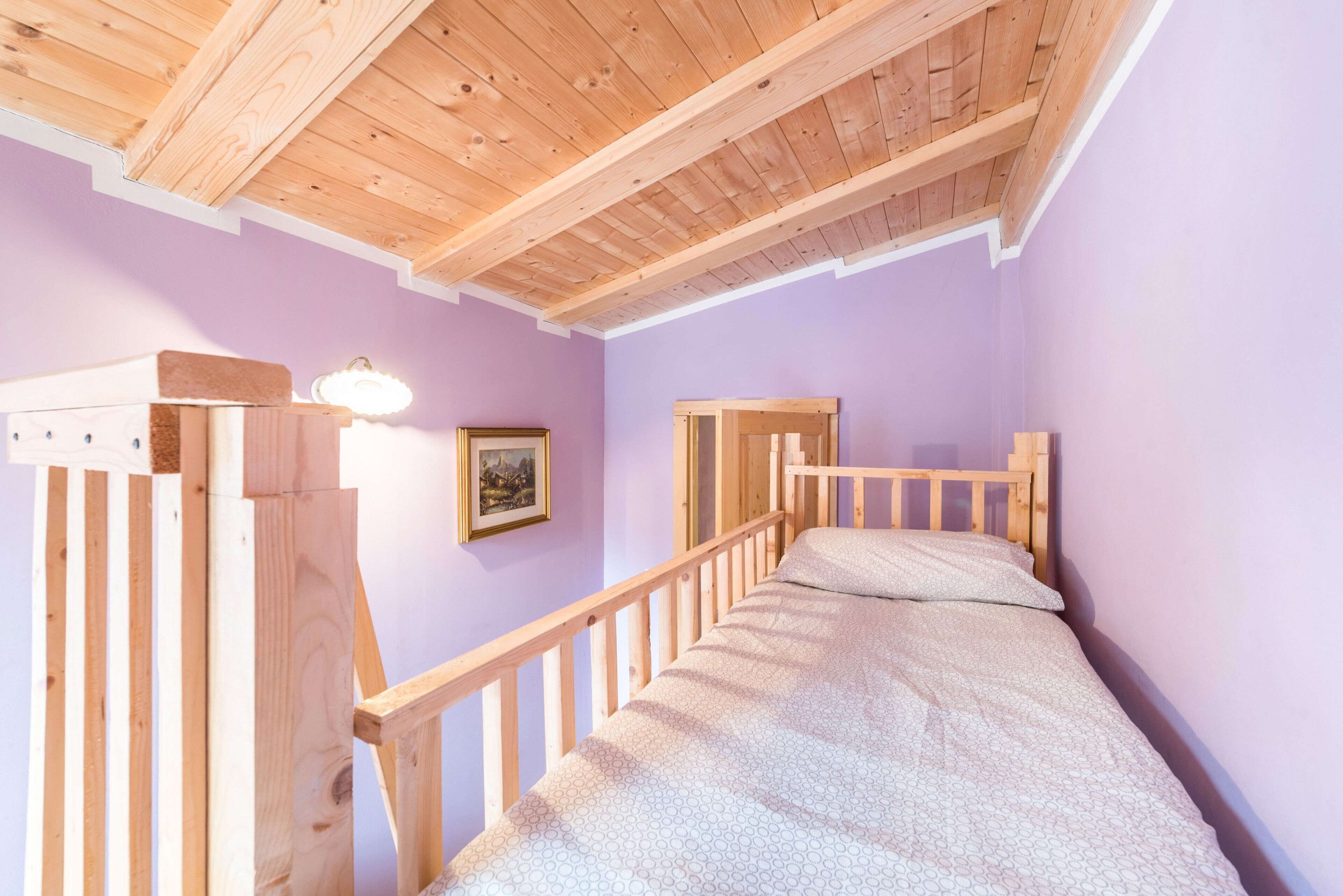 A room with a wooden bunk bed, a single bed, a wooden ceiling, and a wall-mounted light fixture.