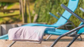 A blue lounge chair with a towel draped over it, positioned outdoors with greenery in the background.