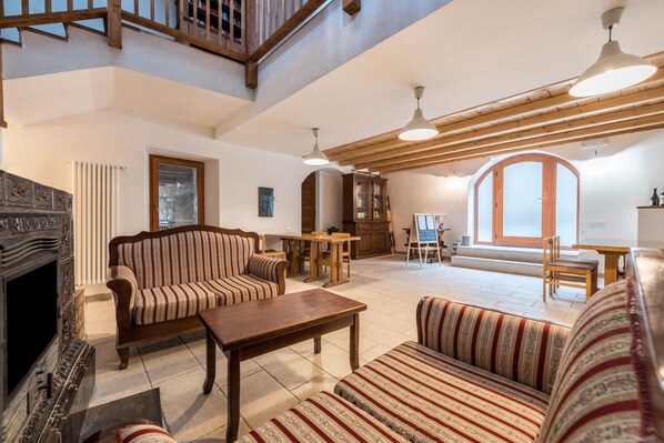 A spacious living area with a fireplace, striped sofas, a wooden coffee table, and a high ceiling with exposed beams.