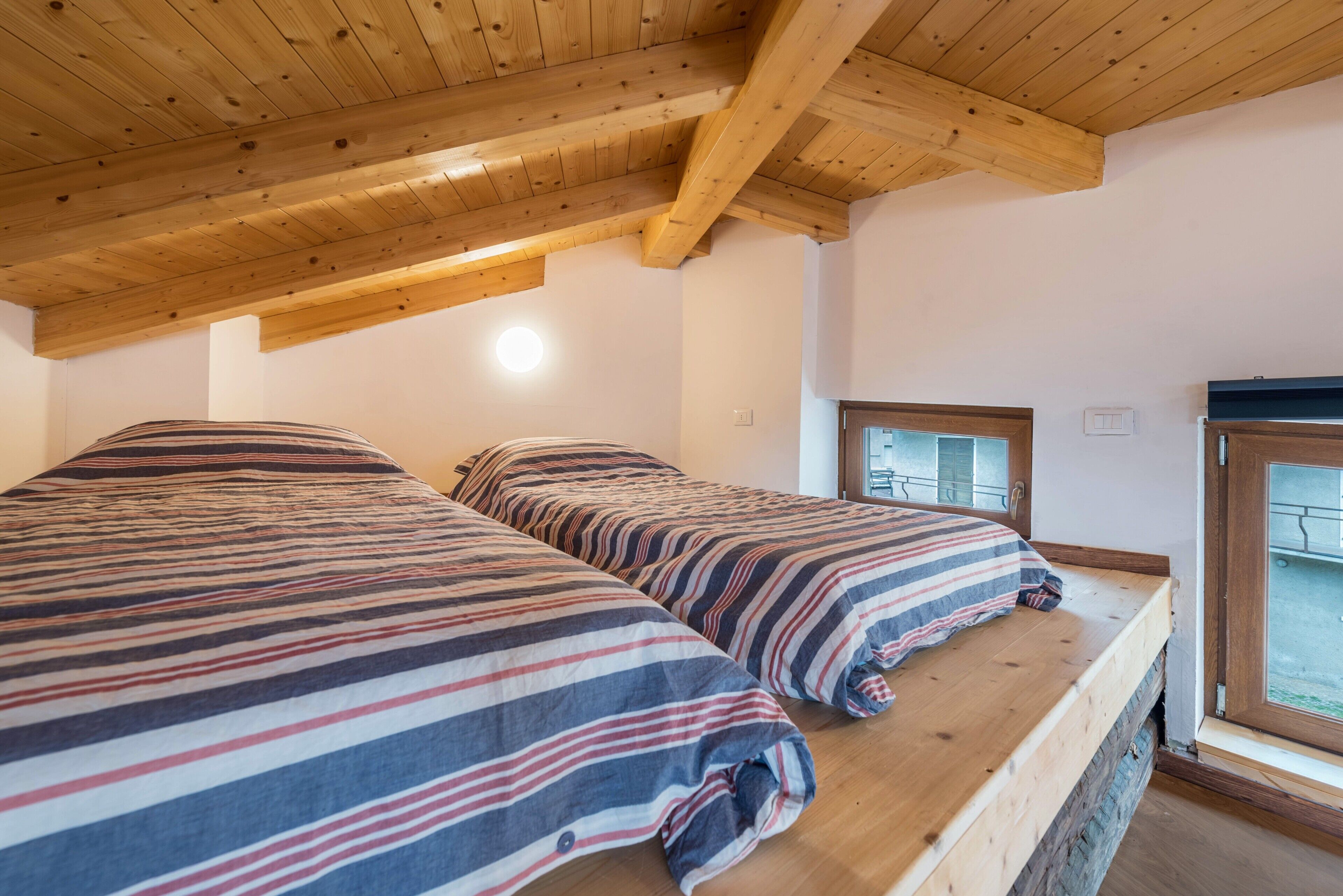 Habitació amb dos llits, bigues de fusta al sostre i una finestra amb vista.