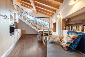A modern interior with a staircase, wooden floors, a sofa with colorful cushions, and a bookshelf.