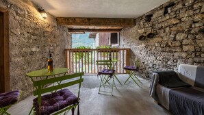 A rustic room with stone walls, a wooden ceiling, a balcony with a view, a table with chairs, and a sofa. - Agriturismo "Al Gallo Nero Giallo" near Lake Garda with Mountain View & Terrace (Tenno)