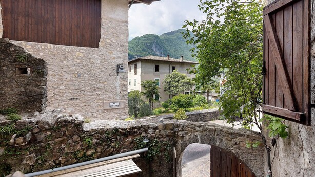 A stone building with a wooden door, a stone wall with a window, and a view of a mountain. - Agriturismo "Al Gallo Nero Giallo" near Lake Garda with Mountain View & Terrace (Tenno)