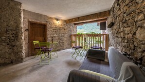 Une pièce rustique avec un mur en pierre, une porte en bois, des chaises pliantes vertes, une petite table et un canapé.