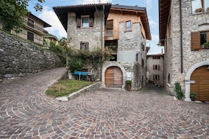 Un bâtiment en pierre doté d’un balcon en bois, d’une cour pavée et d’un mur en pierre.