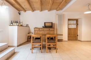 Une pièce avec un plafond en bois, une table en bois avec deux chaises, un téléviseur et une porte sur laquelle est fixé un tableau d’affichage.