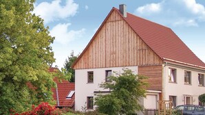 Et toetagers hus med rødt tag og træbeklædning, omgivet af grøn vegetation og et træhegn.