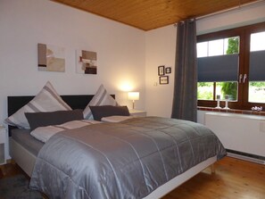 Une chambre à coucher comprenant un lit, une table de chevet, une lampe, une fenêtre avec des rideaux et des œuvres d’art murales.