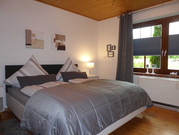 Une chambre à coucher comprenant un lit, une table de chevet, une fenêtre avec des rideaux et des œuvres d’art murales.