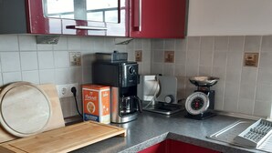 Cozinha com armários vermelhos, tábua de corte de madeira, cafeteira, balança e uma caixa de chocolate Brandi.