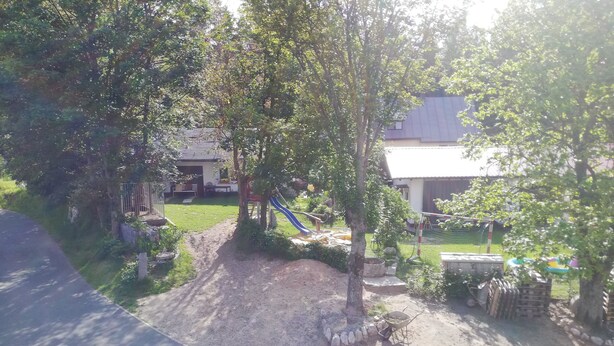 Uma área residencial com um parquinho, uma trilha de terra e uma casa com telhado cinzento.