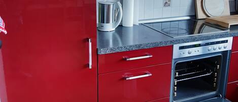 Une cuisine avec des meubles de couleur rouge, une bouilloire en acier inoxydable, un rouleau d’essuie-tout et une planche à découper en bois.